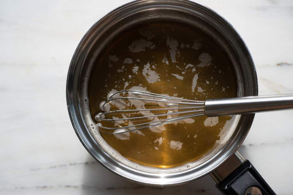 A saucepan filled with hot, clear vanilla simple syrup after sugar has fully dissolved in water, ready to cool for use.