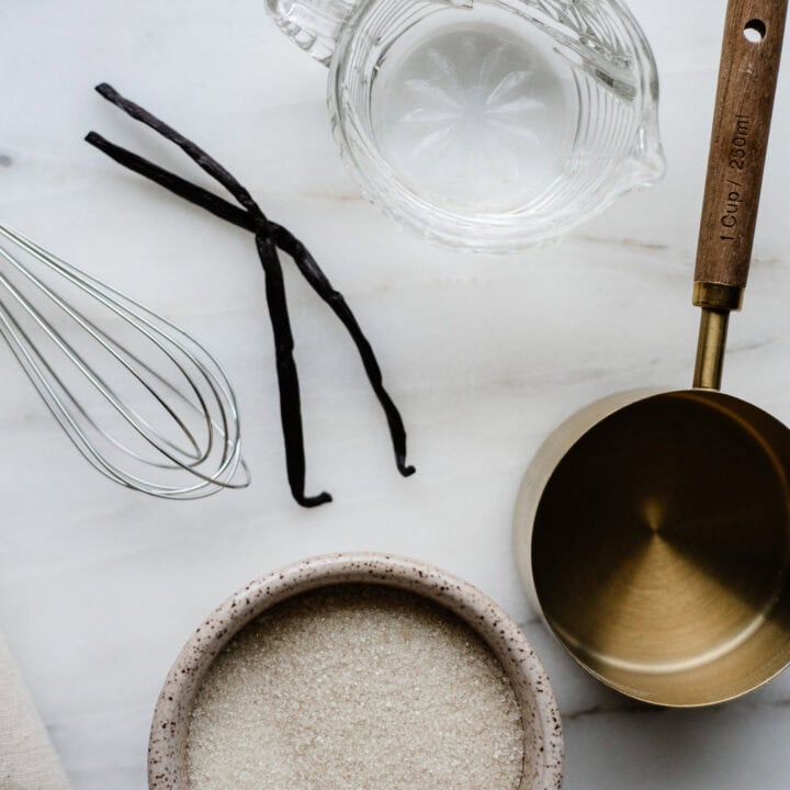 sugar, whisk, measuring cup, water and vanilla beans on a clean surface