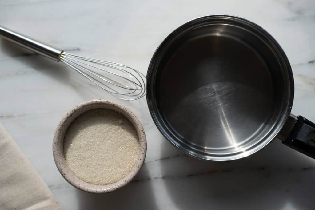 Simple ingredients, sugar, water, and basic tools ready to make homemade vanilla simple syrup.