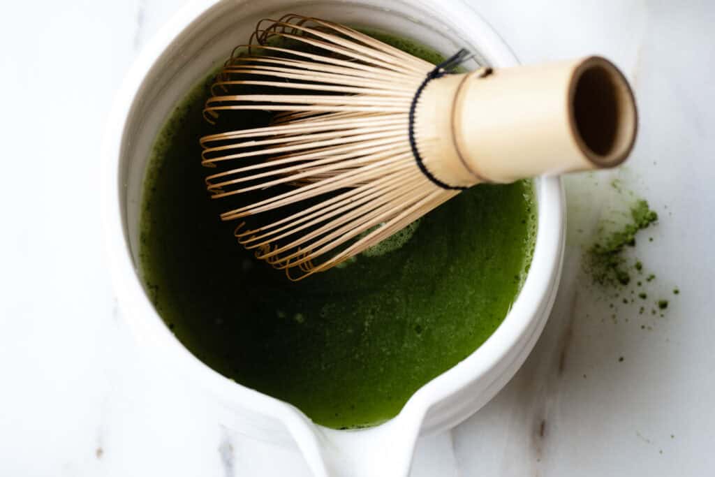green matcha being whisked by a bamboo whisk