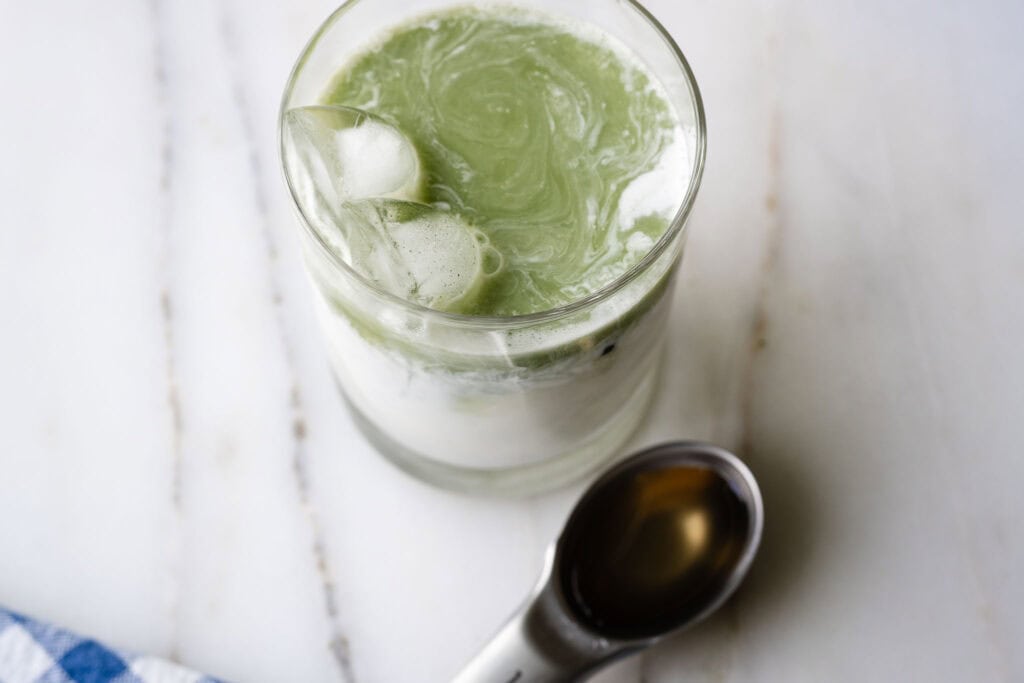 glass with milk and matcha, and sweetener on the side