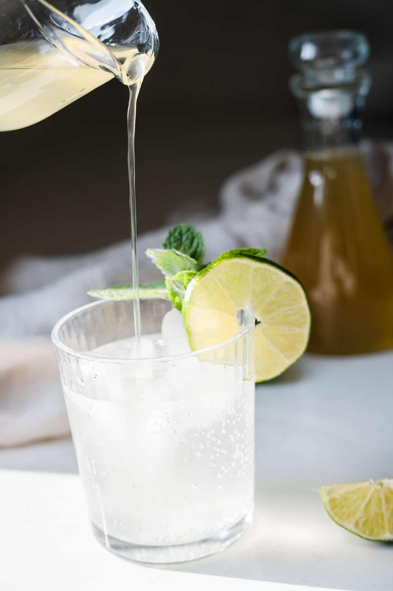 lime simple syrup being poured into a sparkling drink