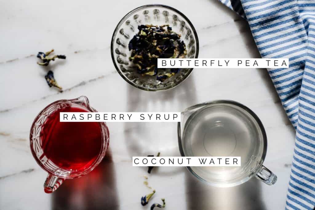 raspberry syrup, coconut water, and butterfly pea tea flowers ready to be made into a drink