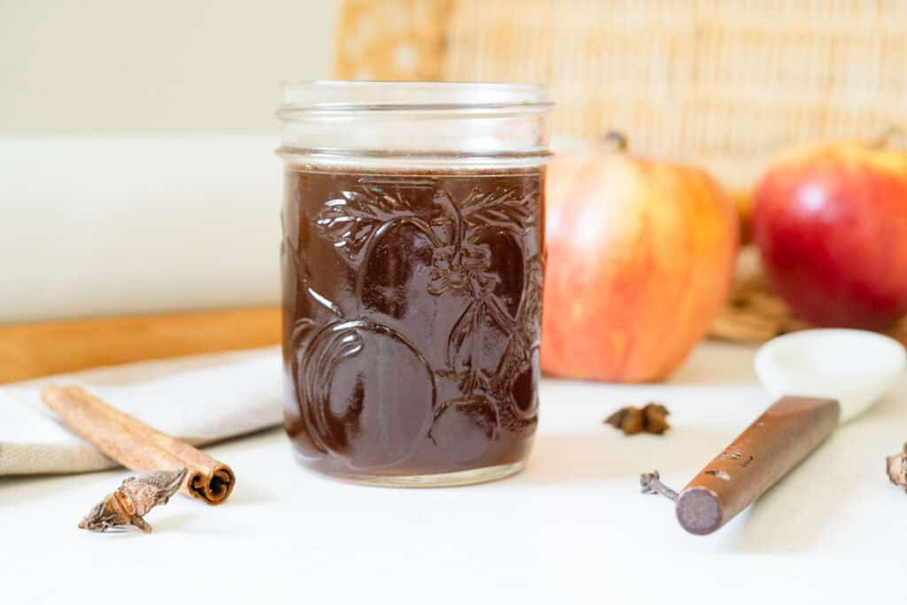 syrup in a jar in front of apples and spices