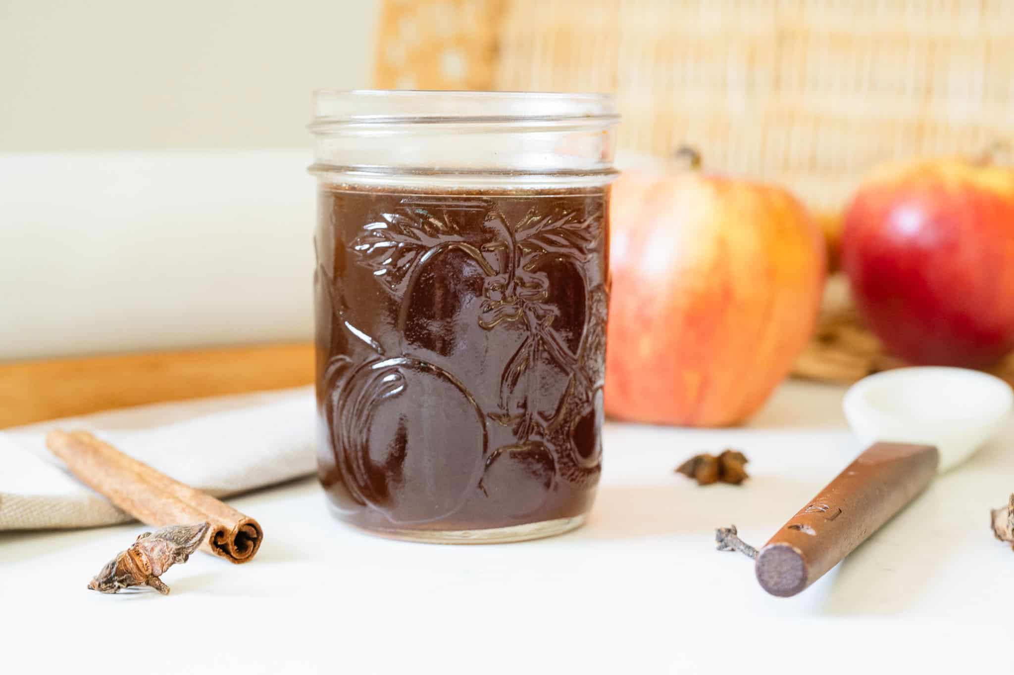 syrup in a jar in front of apples and spices