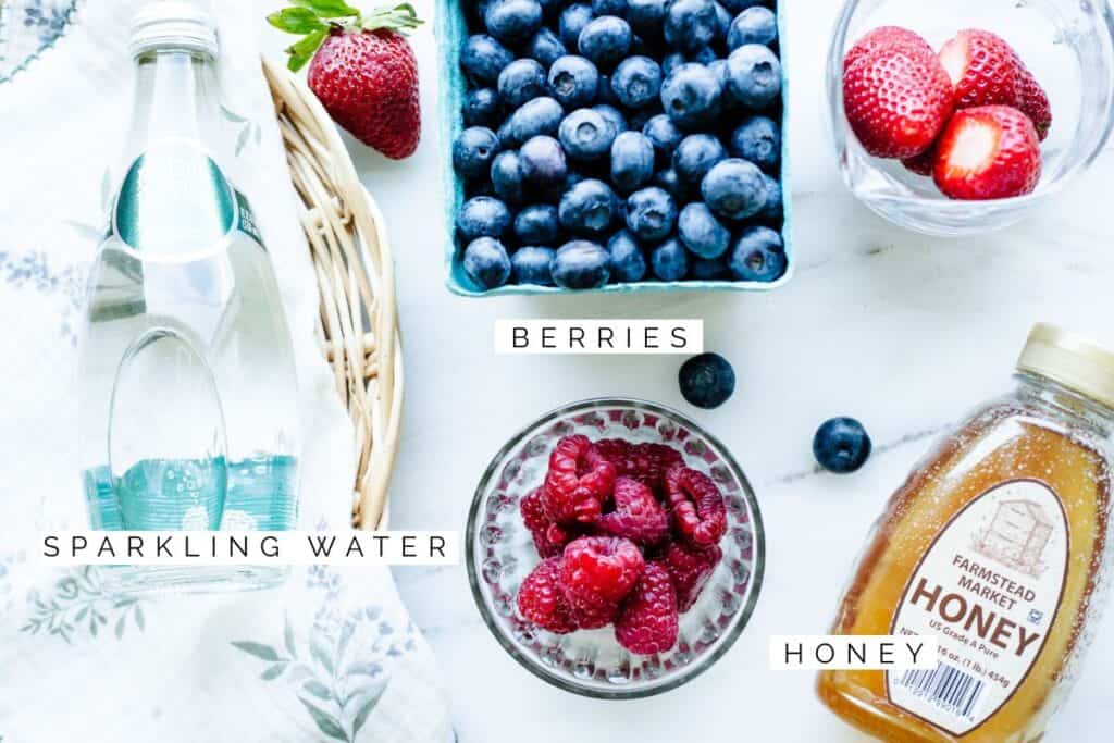 sparkling water, berries, and honey on a counter