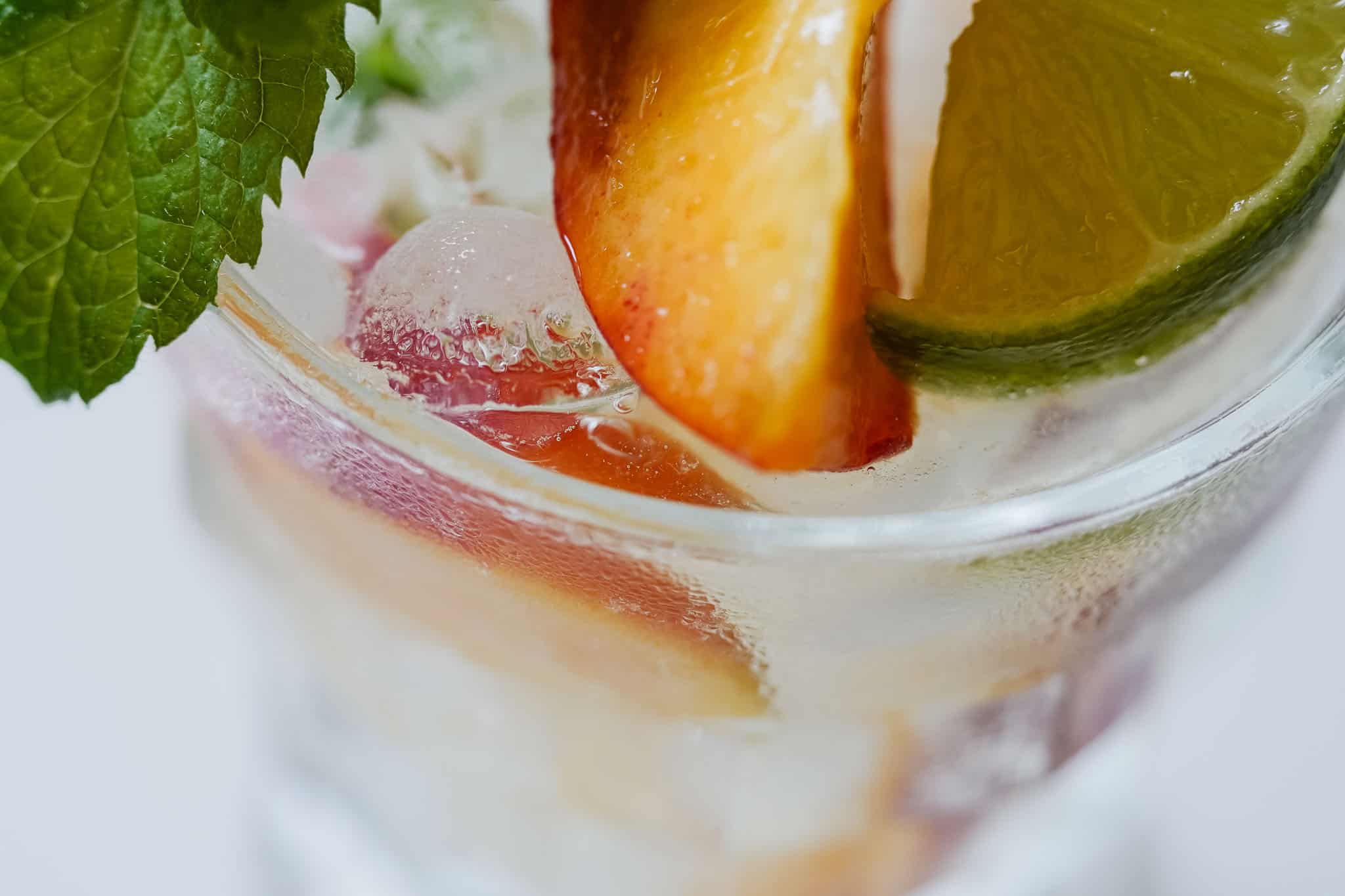 peach, mint, and lime in a cup with ice and sparkling water