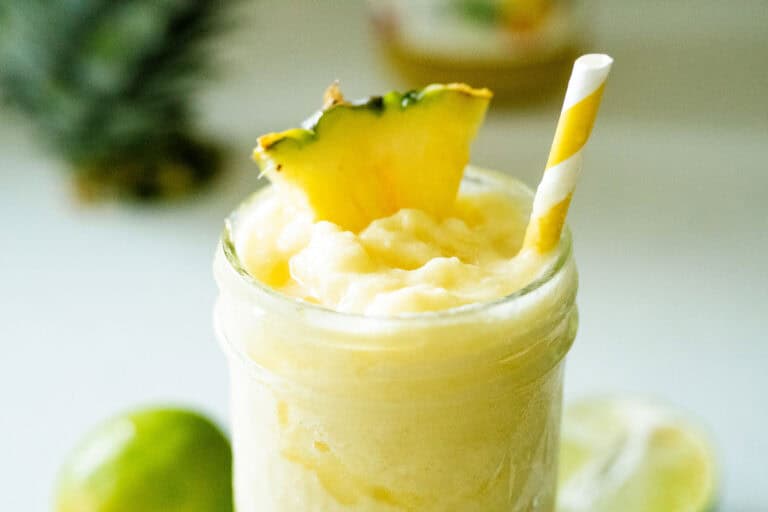 pineapple slushie in a jar with a pineapple wedge and a yellow straw on top