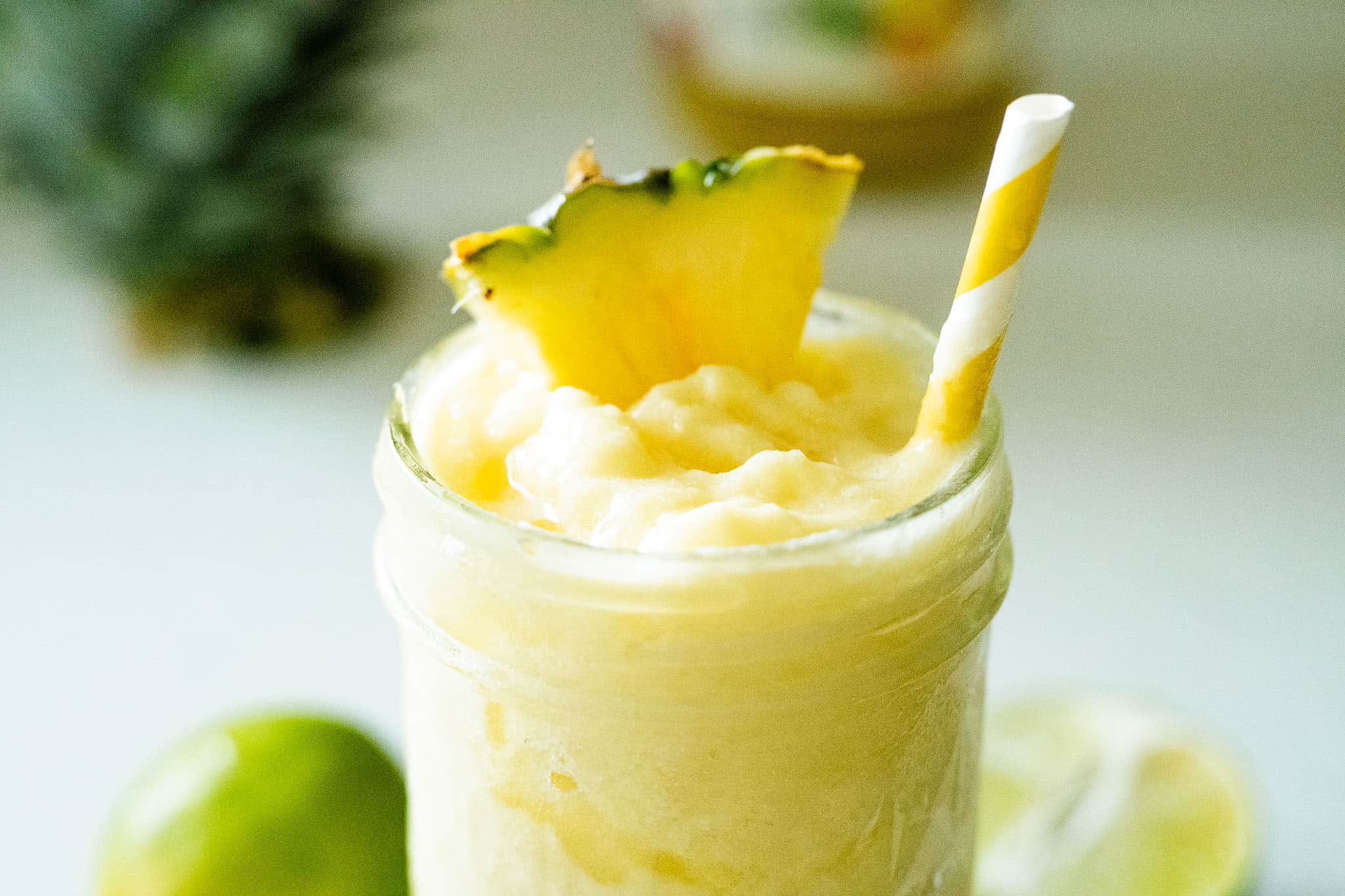 pineapple slushie in a jar with a pineapple wedge and a yellow straw on top
