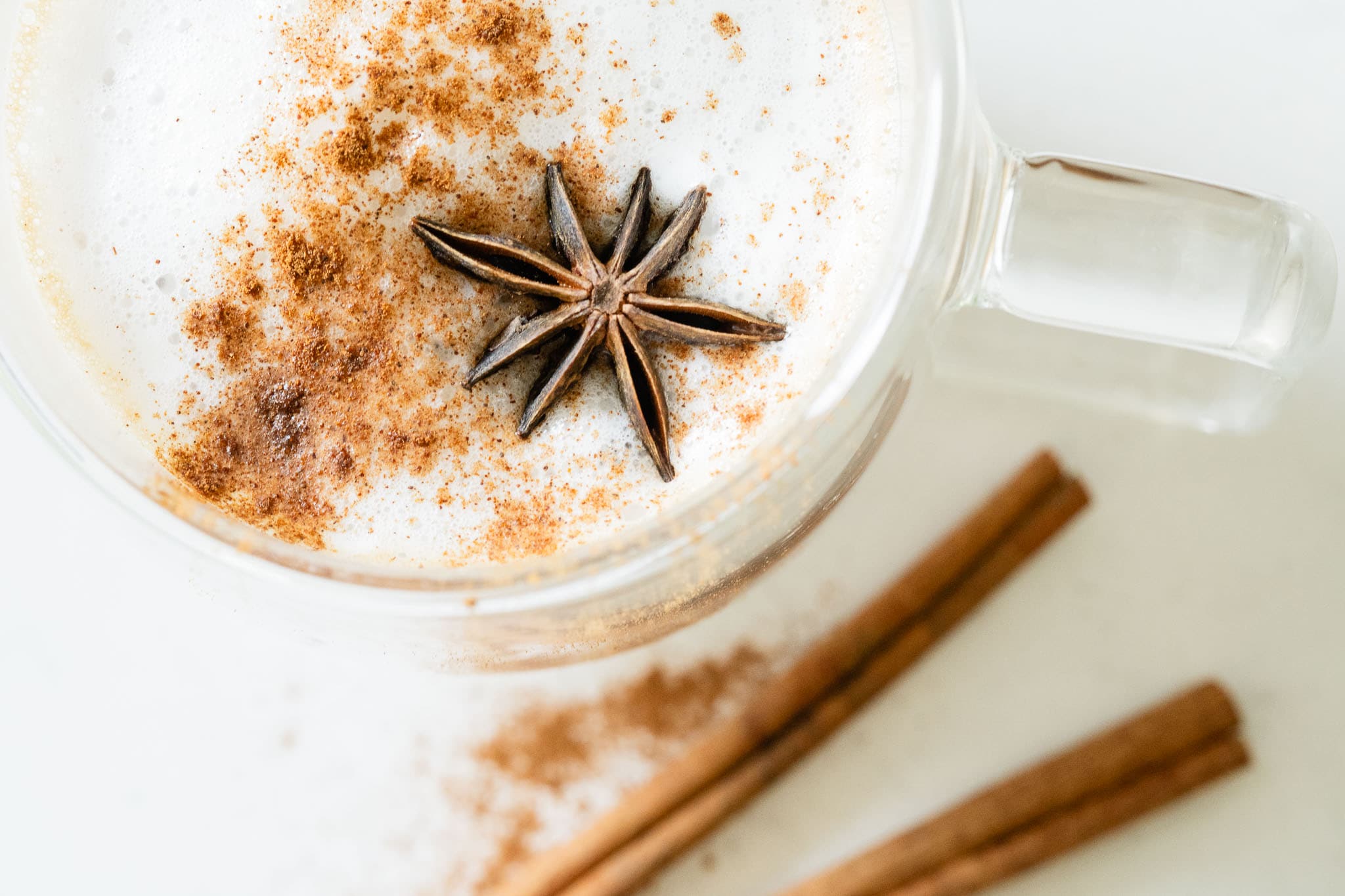 brown drink in a glass mug, topped with steamed milk and spices