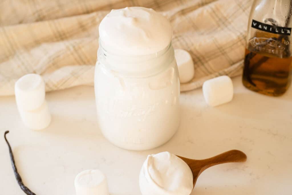 jar with marshmallow fluff surrounded by a scoop and vanilla beans