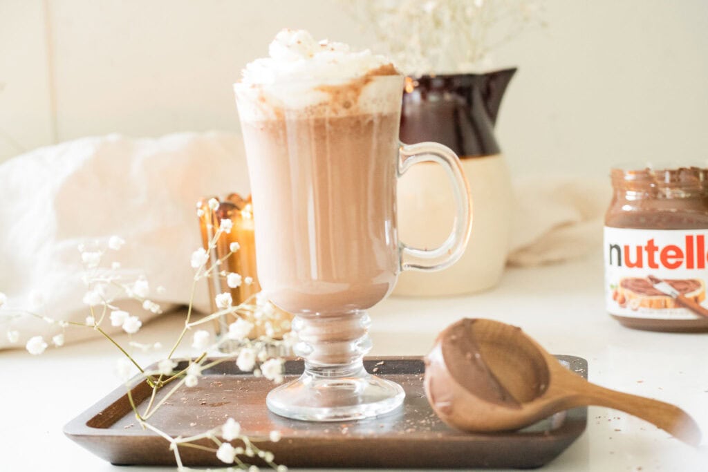 hot chocolate in a glass mug topped with whipped cream with nutella beside it