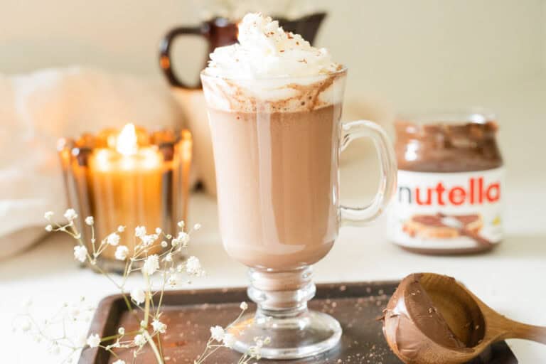 hot chocolate in a glass mug topped with whipped cream with nutella beside it