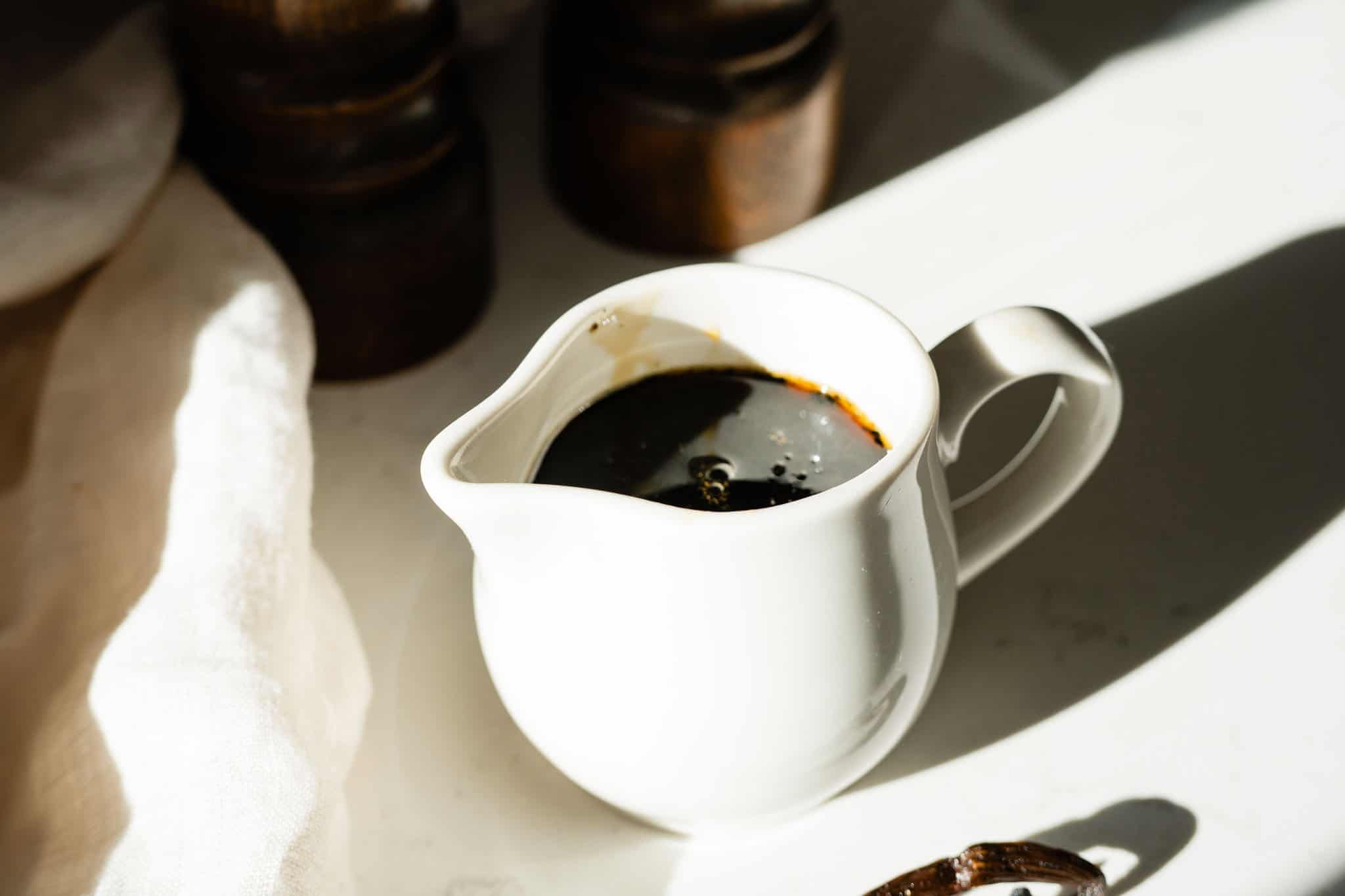 small white pitcher with syrup with a vanilla bean on the side